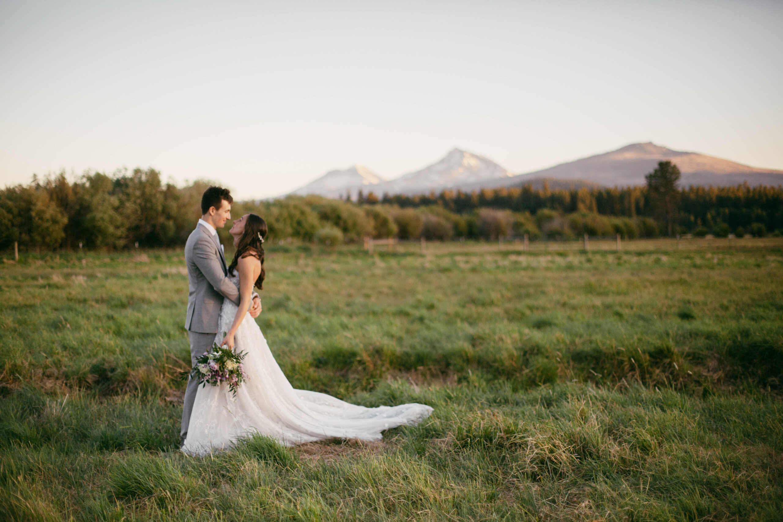 Black Butte summertime wedding in Central Oregon with views of the three sisters mountains in the background of a couple standing together in a field.